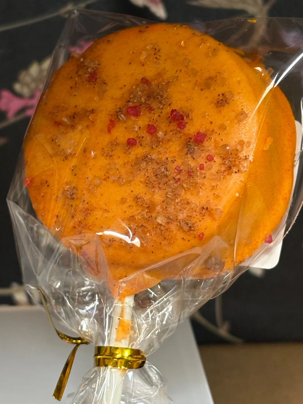 A wrapped golden orange round treat with a sprinkled topping.